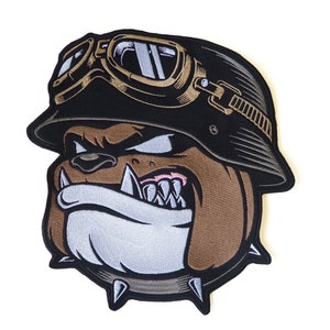 Puede incluir: Un bulldog marrón con un casco negro con gafas doradas y un collar con tachuelas. El bulldog tiene una expresión feroz con los dientes descubiertos.