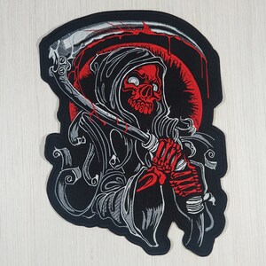 Op de afbeelding: Zwarte en rode geborduurde patch van de Grim Reaper die een zeis vasthoudt. De Grim Reaper draagt een kapmantel en heeft een schedelgezicht. De achtergrond is zwart met een rode cirkel.