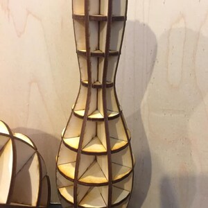 Pode incluir: Um vaso de madeira em forma de pino de boliche com um design geom&eacute;trico. O vaso &eacute; feito de v&aacute;rias pe&ccedil;as de madeira que s&atilde;o unidas para criar uma estrutura de treli&ccedil;a. O vaso &eacute; de cor marrom claro e tem um acabamento de madeira natural.
