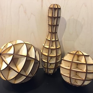 Pode incluir: Tr&ecirc;s formas geom&eacute;tricas de madeira, uma esfera, um pino de boliche e outra esfera, todas de madeira e com um design de treli&ccedil;a.
