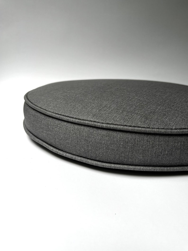May include: A round gray fabric chair cushion with a thick, stitched edge.