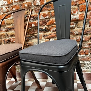 May include: Two metal chairs with curved backrests and four legs. One chair is matte black with a dark gray upholstered seat cushion, and the other is a metallic bronze color with a brown upholstered seat cushion.