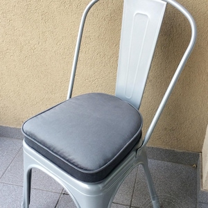 May include: A silver metal chair with a high backrest and a thick, square-shaped dark gray seat cushion. The chair features a smooth, metallic finish and a sturdy frame with four legs, providing a clean and functional seating option.