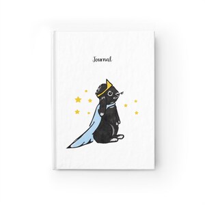 May include: White journal with the word "Journal" at the top. The cover features a cartoon black rabbit wearing a gold crown and a light blue cape, surrounded by yellow stars.