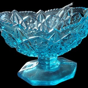 May include: A vintage, light blue glass candy dish with a diamond-cut pattern. The dish has a scalloped rim and sits on a hexagonal base. The glass is a vibrant, transparent blue, perfect for displaying small treats.