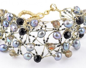 May include: A gold wire bracelet with a delicate design featuring black, gray, and iridescent beads.