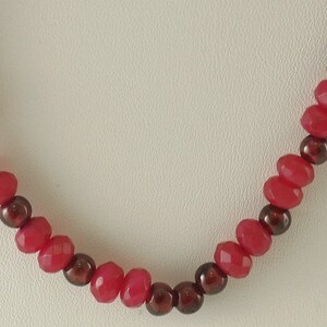 May include: A red and brown beaded necklace with alternating red and brown beads. The necklace is made of faceted red beads and round brown beads.