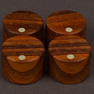 May include: Four small, round wooden boxes with a rich, dark brown grain pattern. Each box has a lighter-coloured, circular inlay on the top. The boxes are arranged in a square formation against a neutral background.