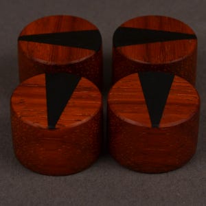 Peut inclure: Quatre objets cylindriques en bois de couleur brun rouge&acirc;tre. Chacun pr&eacute;sente une incrustation noire, triangulaire ou trap&eacute;zo&iuml;dale sur la surface sup&eacute;rieure. Ils sont dispos&eacute;s en carr&eacute; sur un fond neutre.