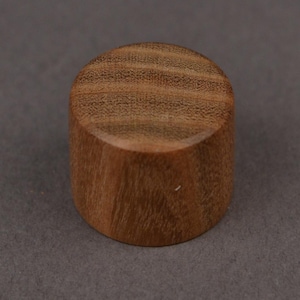 Peut inclure: Petit objet cylindrique en bois, avec un dessus et un dessous plats. Le bois est d'un brun chaud naturel et présente des motifs de grain visibles. L'objet est probablement un élément décoratif ou un petit bouchon.
