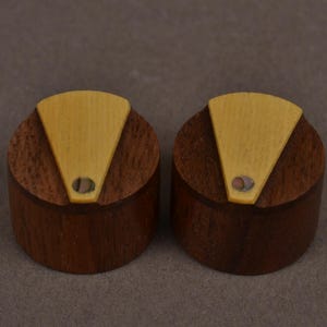 May include: Two cylindrical knobs crafted from dark brown wood, each featuring a triangular light-coloured wooden inlay on the top surface. A small, circular, iridescent shell-like accent is embedded at the tip of each triangular inlay.