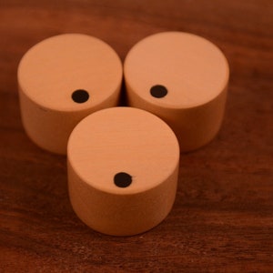Op de afbeelding: Drie houten knoppen met een zwarte stip in het midden van elk. De knoppen zijn lichtbruin en zijn in een driehoekige vorm gerangschikt.