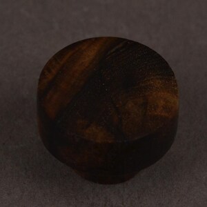 May include: A small, round cabinet knob crafted from dark brown wood with a visible, swirling natural grain pattern. The knob features a smooth, polished surface and a cylindrical base that tapers slightly towards the bottom attachment point.