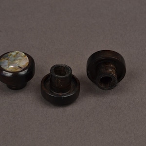May include: Three dark brown wooden cabinet knobs. One knob has a round, inlaid, iridescent shell design. The other two knobs are plain with a mushroom-like shape. These knobs are suitable for furniture restoration or DIY projects.