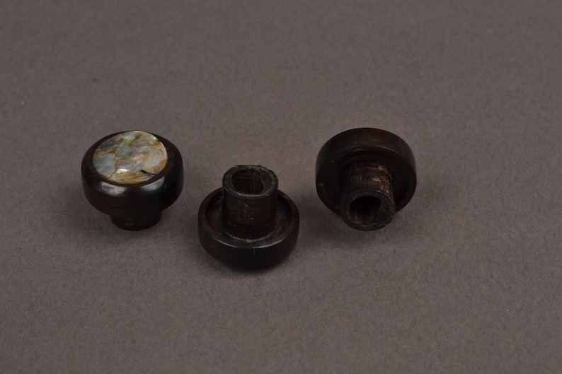 May include: Three dark brown wooden cabinet knobs. One knob has a round, inlaid, iridescent shell design. The other two knobs are plain with a mushroom-like shape. These knobs are suitable for furniture restoration or DIY projects.