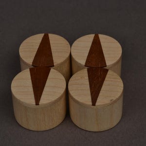 May include: Four wooden place card holders. Each holder is cylindrical with a light wood finish and a dark brown, triangular inlay. The holders are arranged in a square formation against a neutral background.
