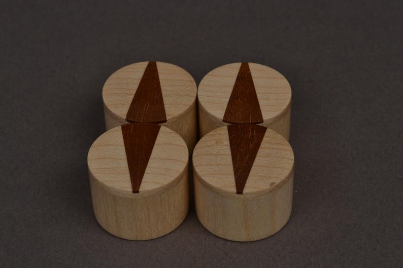 May include: Four wooden place card holders. Each holder is cylindrical with a light wood finish and a dark brown, triangular inlay. The holders are arranged in a square formation against a neutral background.