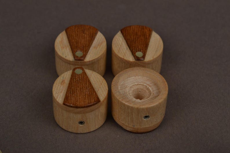 May include: A set of four cylindrical wooden knobs featuring a light-colored wood body with a darker, triangular wood inlay on the top surface. Each knob includes a small circular metal insert on the side for attachment and a central hole.