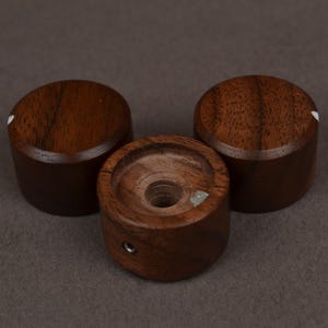 Pu&ograve; includere: Tre manopole in legno marrone scuro con un punto indicatore bianco. Le manopole sono cilindriche con una parte superiore e inferiore piatte. Una manopola ha un foro al centro. Le manopole sono probabilmente per un'apparecchiatura audio.