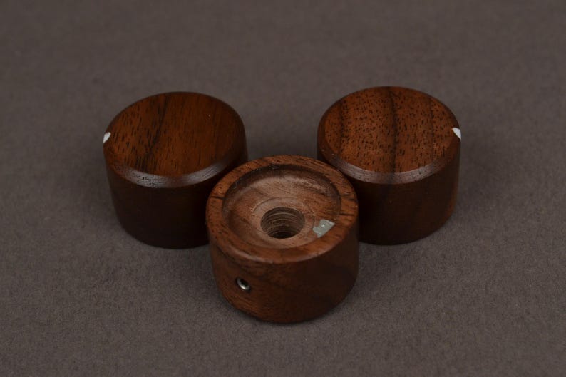 Pu&ograve; includere: Tre manopole in legno marrone scuro con un punto indicatore bianco. Le manopole sono cilindriche con una parte superiore e inferiore piatte. Una manopola ha un foro al centro. Le manopole sono probabilmente per un'apparecchiatura audio.