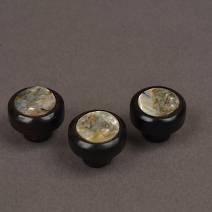 May include: Three dark brown cabinet knobs with a round, iridescent, mother-of-pearl inlay. The knobs have a classic, rounded shape and are set against a neutral background. These decorative knobs are suitable for furniture.