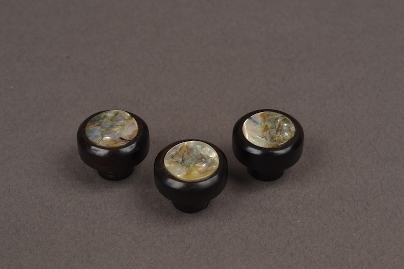 May include: Three dark brown cabinet knobs with a round, iridescent, mother-of-pearl inlay. The knobs have a classic, rounded shape and are set against a neutral background. These decorative knobs are suitable for furniture.