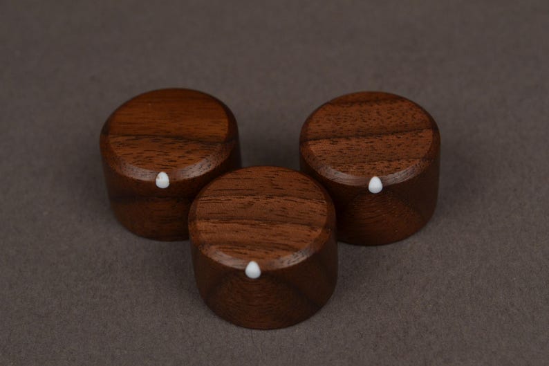 Pu&ograve; includere: Tre pomelli in legno marrone scuro, ciascuno con un piccolo punto bianco. I pomelli sono cilindrici e realizzati in legno. Sono disposti a triangolo. La venatura del legno &egrave; visibile sulle superfici superiori.