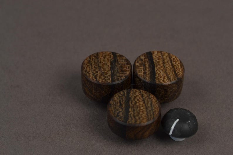 Pode incluir: Tr&ecirc;s bot&otilde;es circulares de madeira com um padr&atilde;o de gr&atilde;o de madeira texturizado em castanho escuro dispostos em forma&ccedil;&atilde;o triangular, acompanhados por um pequeno bot&atilde;o preto com uma linha vertical branca na superf&iacute;cie superior.