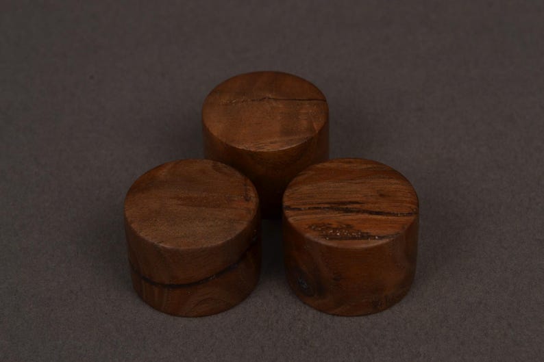 K&ouml;nnte beinhalten: Drei zylindrische Holzobjekte in satten Braunt&ouml;nen mit sichtbarer Maserung. Sie sind in einer Gruppe angeordnet, zwei gestapelt und eines leicht erh&ouml;ht, vor einem neutralen Hintergrund.