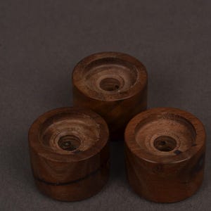 K&ouml;nnte beinhalten: Drei handgefertigte Kerzenhalter aus Holz. Jeder Halter ist zylindrisch mit einer kreisf&ouml;rmigen Vertiefung oben, um eine Kerze aufzunehmen. Das Holz hat eine satte, dunkelbraune Farbe und sichtbare Maserung. Die Halter sind in Dreiecksform angeordnet.