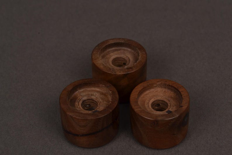 K&ouml;nnte beinhalten: Drei handgefertigte Kerzenhalter aus Holz. Jeder Halter ist zylindrisch mit einer kreisf&ouml;rmigen Vertiefung oben, um eine Kerze aufzunehmen. Das Holz hat eine satte, dunkelbraune Farbe und sichtbare Maserung. Die Halter sind in Dreiecksform angeordnet.