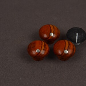 May include: Three round wooden knobs with a polished reddish-brown grain pattern and a small silver circular inlay on the top, accompanied by one black knob featuring a single white vertical line indicator on its surface.