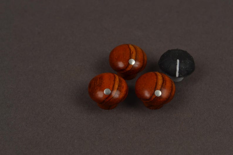May include: Three round wooden knobs with a polished reddish-brown grain pattern and a small silver circular inlay on the top, accompanied by one black knob featuring a single white vertical line indicator on its surface.