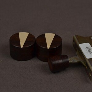 Puede incluir: Dos perillas cil&iacute;ndricas de madera de color marr&oacute;n oscuro con una incrustaci&oacute;n triangular de color claro en la parte superior, colocadas junto a un componente mec&aacute;nico de metal con una perilla de madera m&aacute;s peque&ntilde;a y una etiqueta blanca con el texto 31993.