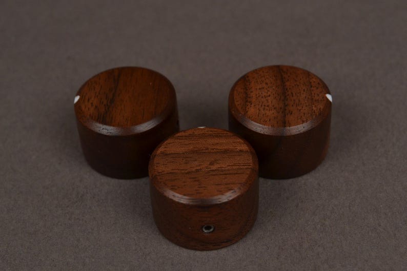 Pu&ograve; includere: Tre manopole in legno marrone scuro, di forma cilindrica e arrotondata. Ognuna ha un punto bianco sulla parte superiore. Sono disposte a triangolo su uno sfondo grigio. Probabilmente per mobili o elettronica.