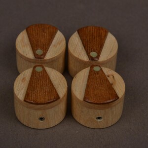 May include: A set of four cylindrical wooden knobs, each featuring a light-colored wood base with a contrasting dark brown triangular inlay on the top surface. Each knob includes a small circular center accent and a metal mounting hole on the side.