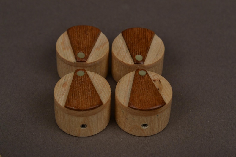 May include: A set of four cylindrical wooden knobs, each featuring a light-colored wood base with a contrasting dark brown triangular inlay on the top surface. Each knob includes a small circular center accent and a metal mounting hole on the side.