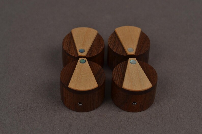 Puede incluir: Cuatro pomos cil&iacute;ndricos de madera marr&oacute;n oscuro, cada uno con una incrustaci&oacute;n triangular de madera beige claro en la superficie superior. Un peque&ntilde;o acento de piedra azul verdosa iridiscente est&aacute; incrustado en la punta de cada tri&aacute;ngulo.