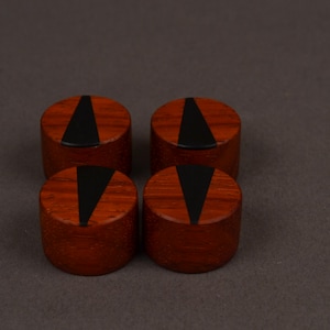 Peut inclure: Quatre objets cylindriques en bois de couleur brun rouge&acirc;tre. Chacun pr&eacute;sente une incrustation triangulaire noire sur la surface sup&eacute;rieure. Ils sont dispos&eacute;s en carr&eacute; sur un fond neutre.