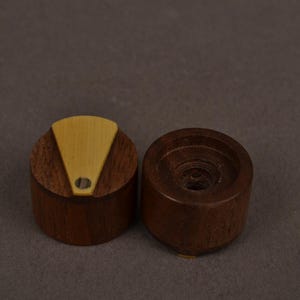Pu&ograve; includere: Due manopole cilindriche in legno marrone scuro. Una manopola presenta un inserto triangolare color beige chiaro sulla superficie superiore con un piccolo foro circolare vicino alla base del triangolo. L'altra manopola &egrave; liscia con un centro cavo.