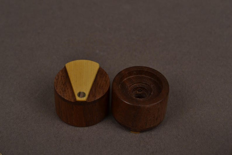 Pu&ograve; includere: Due manopole cilindriche in legno marrone scuro. Una manopola presenta un inserto triangolare color beige chiaro sulla superficie superiore con un piccolo foro circolare vicino alla base del triangolo. L'altra manopola &egrave; liscia con un centro cavo.