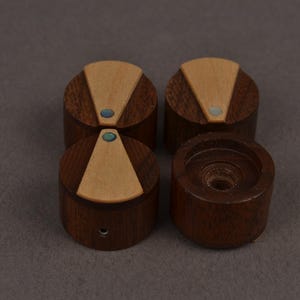Puede incluir: Cuatro perillas cil&iacute;ndricas de madera con una base de madera marr&oacute;n oscura y una incrustaci&oacute;n triangular de madera clara en la parte superior. Cada perilla incluye un peque&ntilde;o acento circular iridiscente en la punta de la incrustaci&oacute;n.