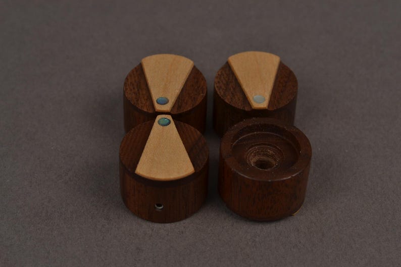 Puede incluir: Cuatro perillas cil&iacute;ndricas de madera con una base de madera marr&oacute;n oscura y una incrustaci&oacute;n triangular de madera clara en la parte superior. Cada perilla incluye un peque&ntilde;o acento circular iridiscente en la punta de la incrustaci&oacute;n.