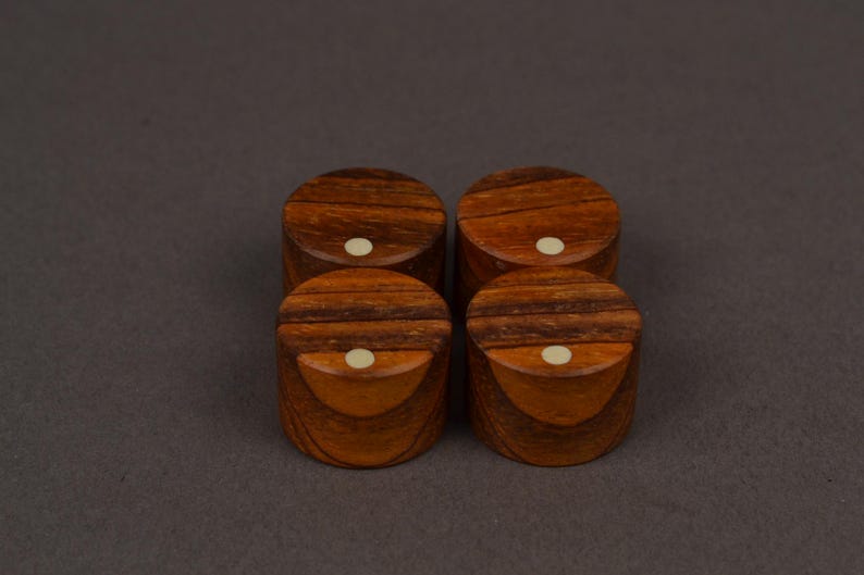 May include: Four small, round wooden boxes with a rich, dark brown grain pattern. Each box has a lighter-colored, circular inlay on the top. The boxes are arranged in a square formation against a neutral background.