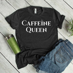 Op de afbeelding: Een donkergrijs t-shirt met de tekst "CAFFEINE QUEEN" in witte letters.