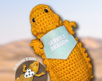 May include: A yellow crocheted bearded dragon wearing a light blue bandana with the text "SERVICE DRAGON" on it. The text "For Bearded Dragons" is visible in the lower left corner of the image.
