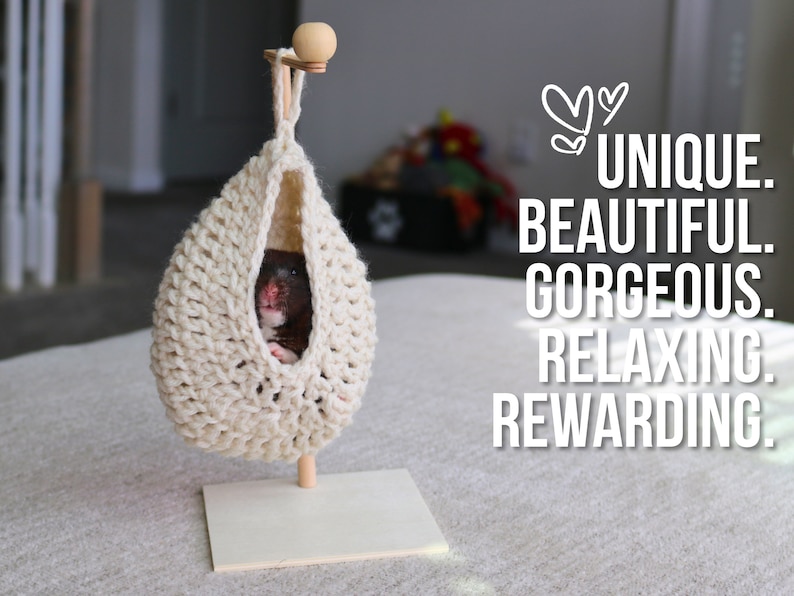 May include: A small hamster resting in a beige crocheted hanging hammock. The hammock is suspended from a wooden stand with a small wooden ball on top.