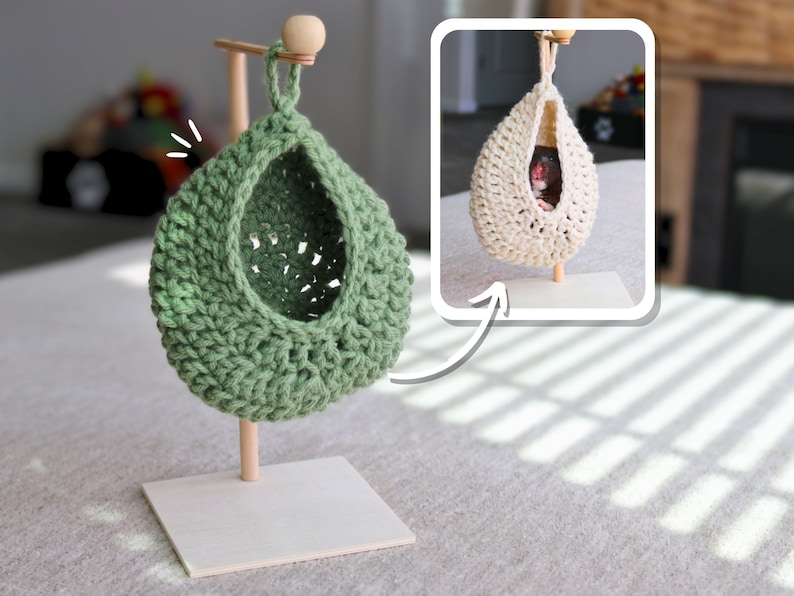 May include: A green crocheted hanging hammock for small pets, like hamsters or gerbils, is shown on a wooden stand. The hammock is suspended from the stand by a wooden dowel. The hammock is made of a soft, crocheted material and has a round shape. The stand is made of wood and has a square base.