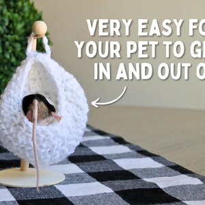 May include: A white crocheted hanging bed for small pets, like a mouse, with a wooden stand. The bed is suspended from a wooden dowel and has a round opening for easy access. The text "VERY EASY FOR YOUR PET TO GET IN AND OUT OF!" is visible in the image.