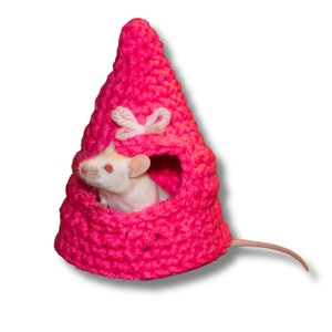 May include: A white rat with pink eyes peeks out of a pink crocheted house shaped like a cone.